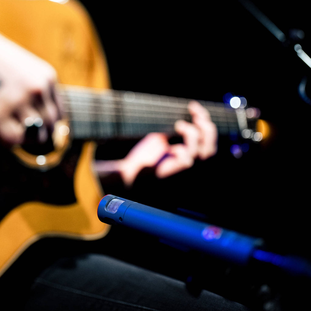 Austrian Audio CC8 condenser microphone with a sleek black body and gold accents, shown on a stand with a pop filter.